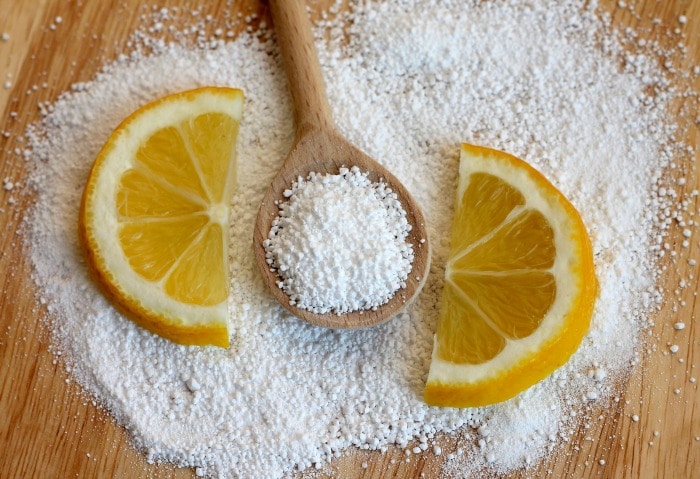 Citric acid next to two lemon slices and a wooden spoon.