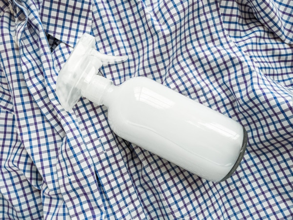 Homemade wrinkle release in a spray bottle laying on top of a wrinkled shirt.