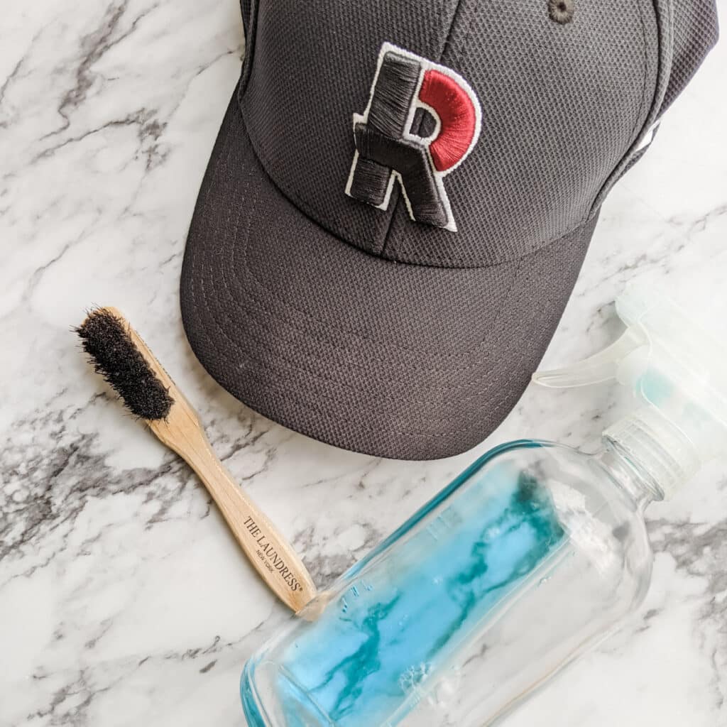 Dirty baseball cap next to a brush and  vinegar soap solution.