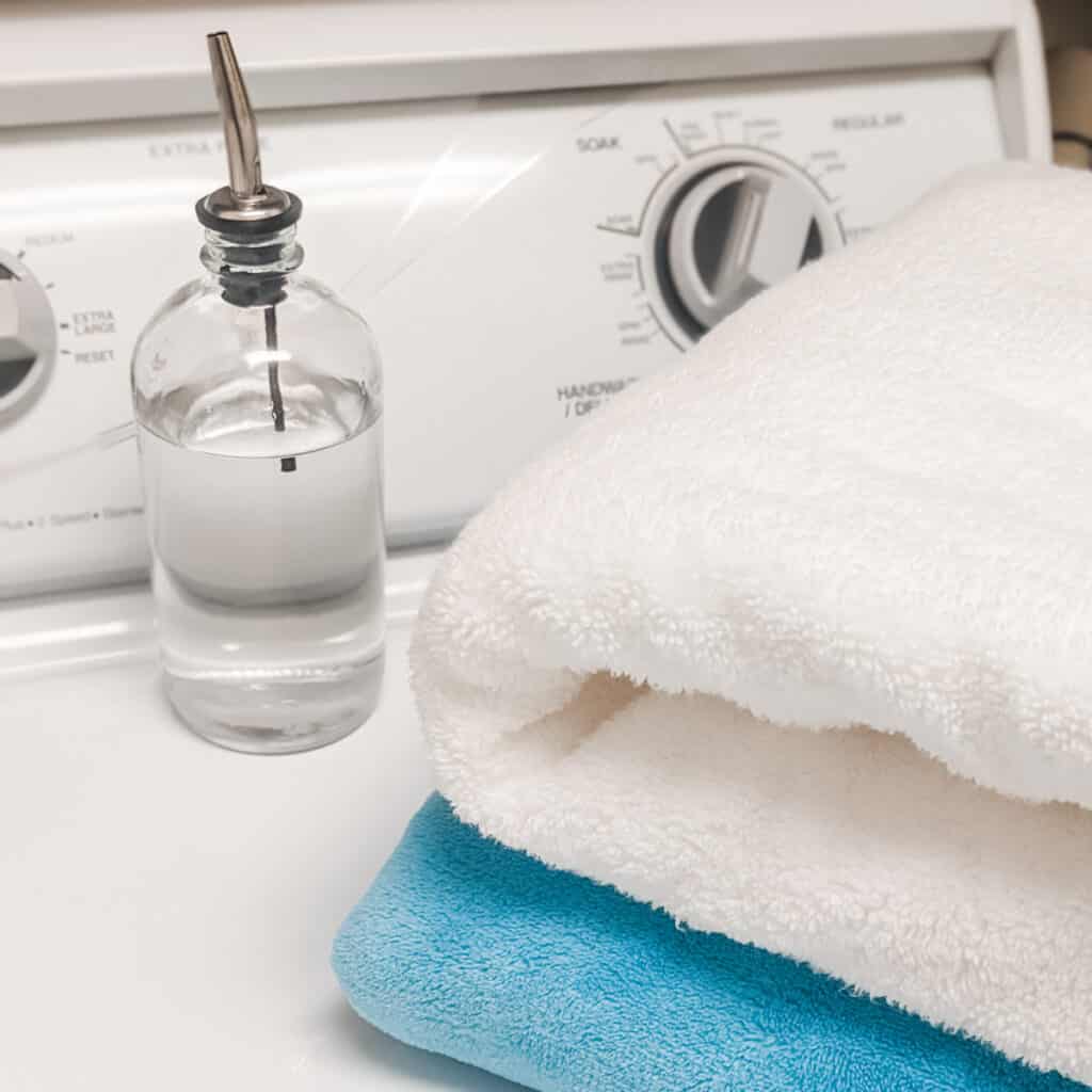 A glass bottle of vinegar next to towels on the washing machine after cleaning to get the mildew smell out.