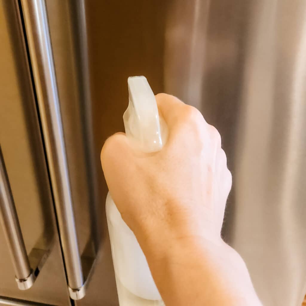 Spraying the lemon vinegar cleaner onto the stainless steel appliance.