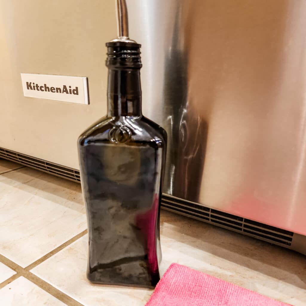 Bottle of olive oil sitting next to stainless steel appliance.