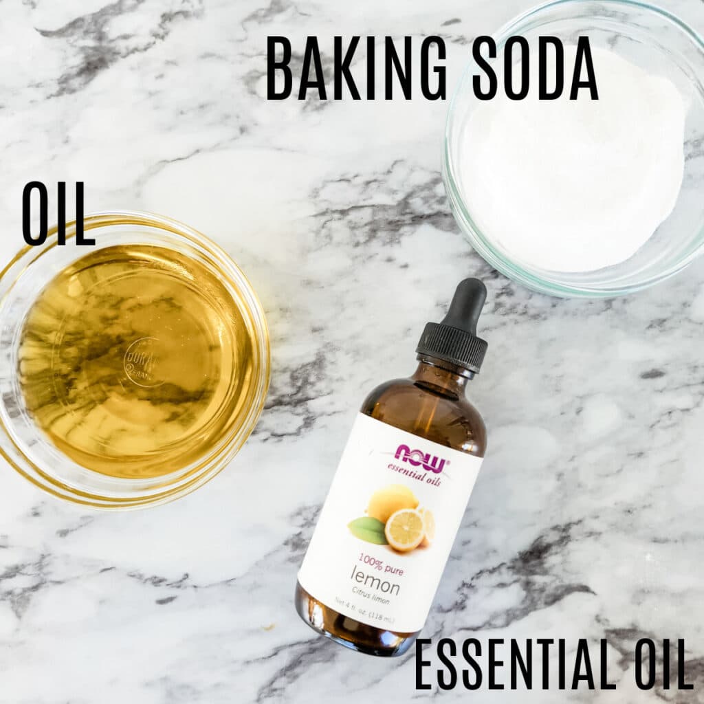 Baking soda in a bowl, next to the vegetable oil in a glass bowl and the bottle of lemon essential oils.