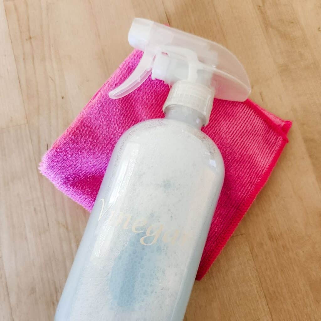 Vinegar in a glass bottle on top of a pink towel, sitting on a butcher block countertop.