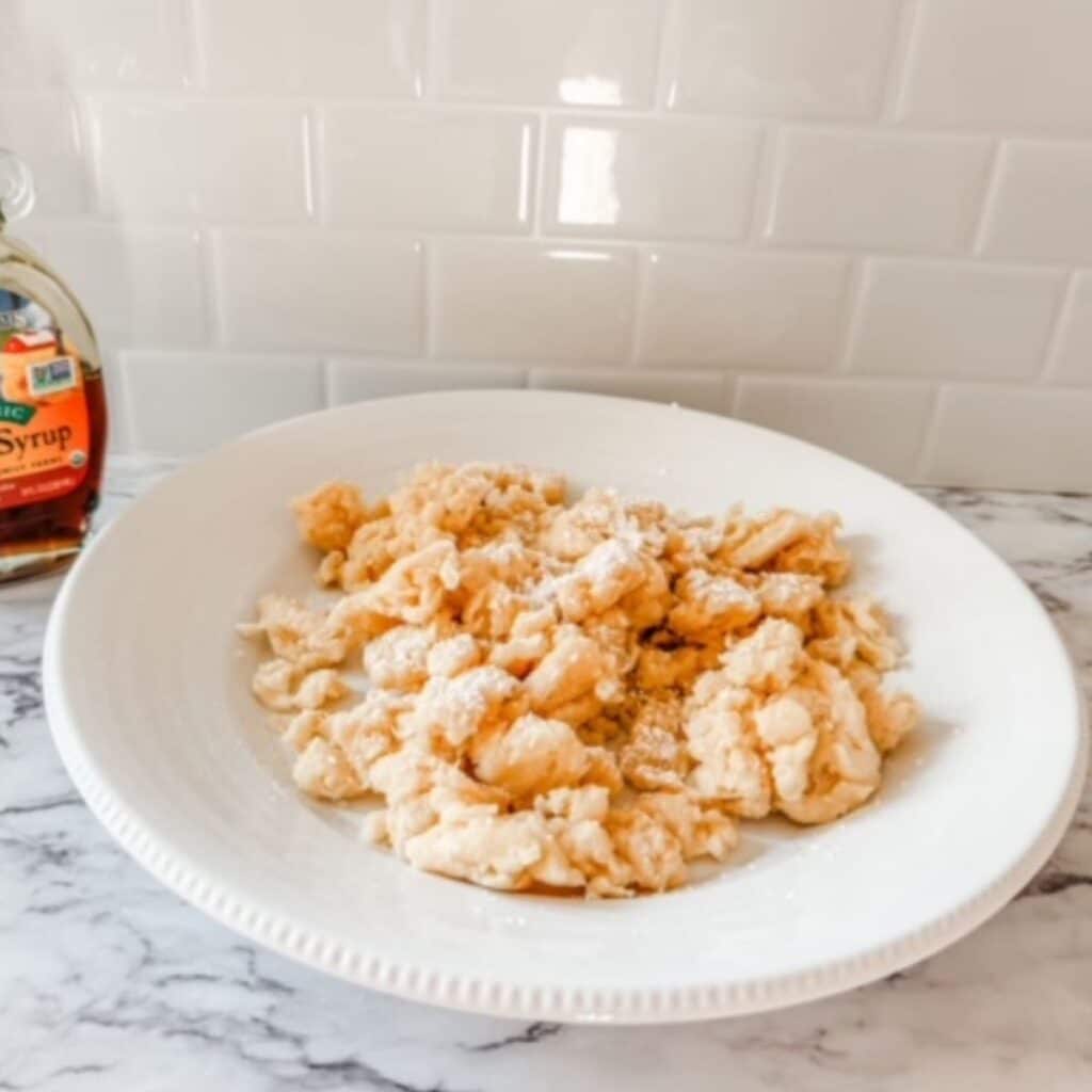 Homemade scrambled pancakes in a white bowl next to syrup.